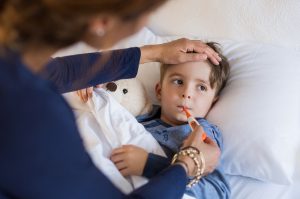 Mutter fühlt die Stirn eines kranken, im Bett liegenden Kindes und steckt ihm ein Fieberthermometer in den Mund