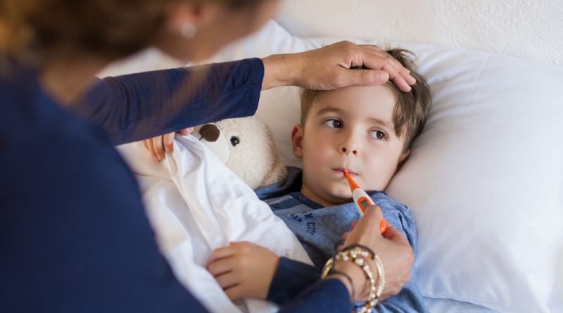 Mutter fühlt die Stirn eines kranken, im Bett liegenden Kindes und steckt ihm ein Fieberthermometer in den Mund
