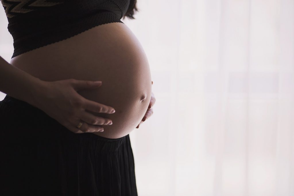 Frau hält sich ihren runden Bauch. 