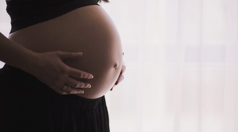 Frau hält sich ihren runden Bauch.